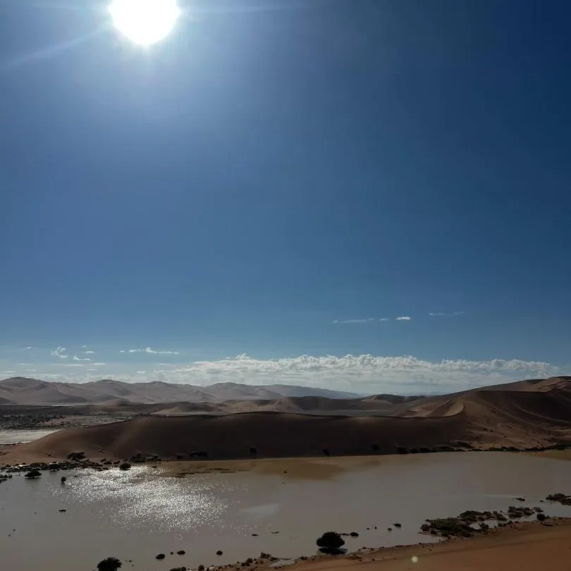 The sun bursting over dunes above a thin sheet of water on the sand