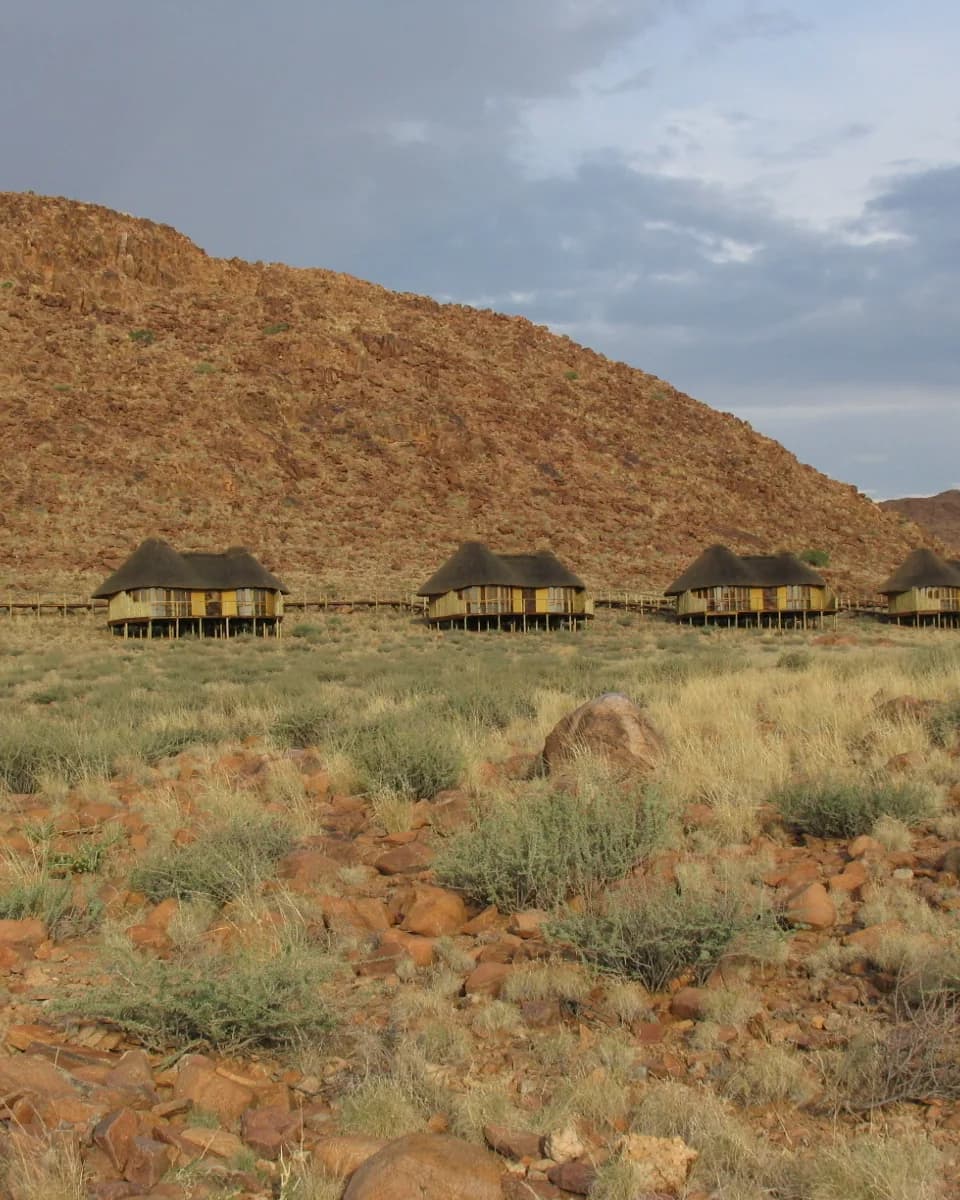 Row of thatched chalets on stilts below a rocky red hillside