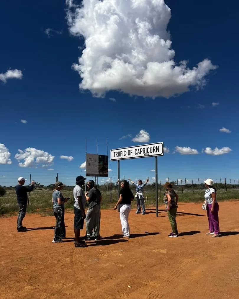 Liger Tours guests gathered around the Tropic of Capricorn roadside sign on red desert soil
