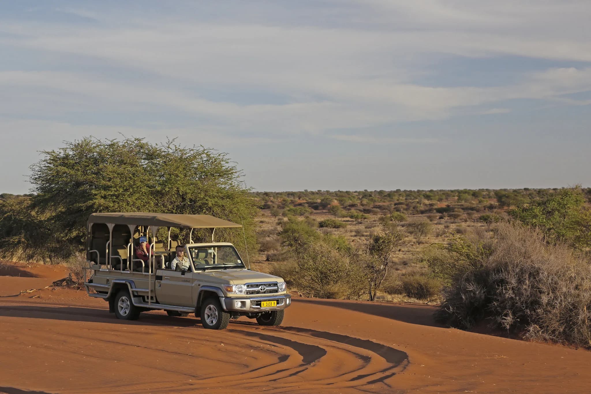 Open safari vehicle crossing red sand at golden hour with dune shadows behind